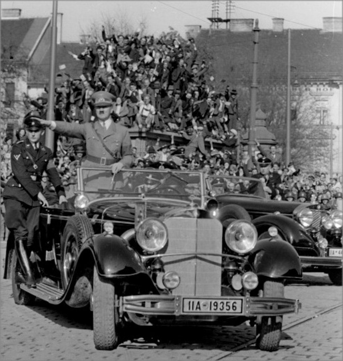 Das Foto zeigt Adolf Hitler mit ausgestrecktem rechen Arm im Auto stehend durch Graz fahren.