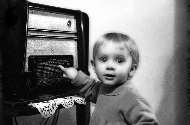 Ein Kleinkind zeigt auf einen Radio und schaut in die Kamera.