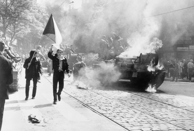 Invasion des Warschauer Pakts in die Tschechoslowakei, 1968 - Prag: Brennende Panzer , Soldaten und zwei Männer in den Straßen von Prag. Ein Mann shwenkt eine tschechische Fahne.