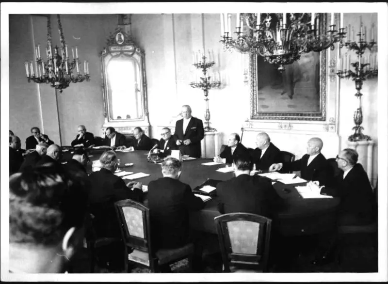 Der erste Ministerrat der neuen Regierung unter Bundeskanzler Alfons Gorbach (ÖVP). Wien, Bundeskanzleramt. Blick auf den großen Tisch, an dem die verschiedenen Politiker sitzen. Nur Alfons Gorbach steht.