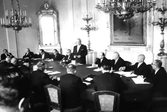 Der erste Ministerrat der neuen Regierung unter Bundeskanzler Alfons Gorbach (ÖVP). Wien, Bundeskanzleramt. Blick auf den großen Tisch, an dem die verschiedenen Politiker sitzen. Nur Alfons Gorbach steht.