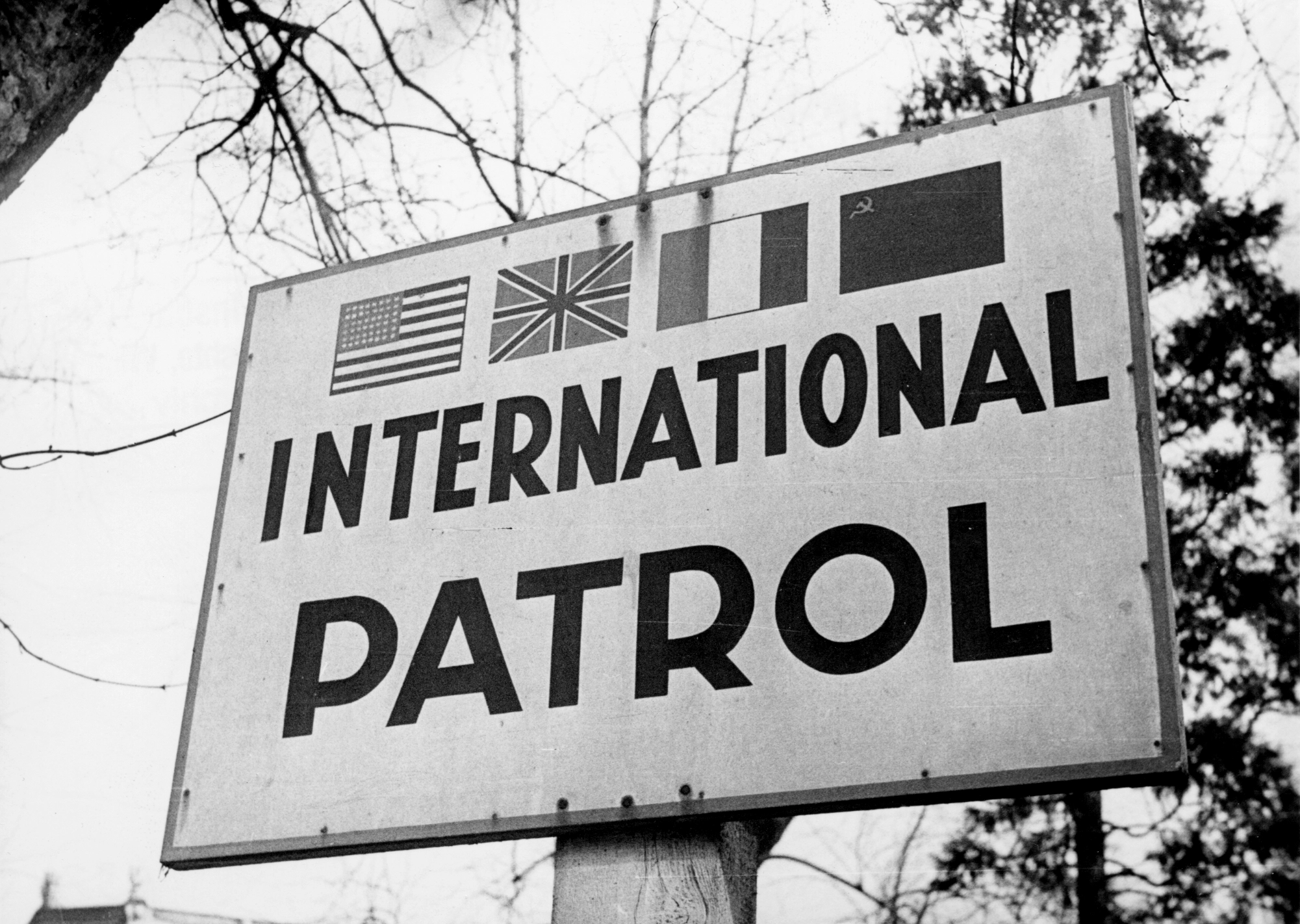 Tafel mit den vier Flaggen der Besatzungsmächte (eher klein gehalten) und darunter groß die Aufschrift "INTERNATIONAL PATROL"
