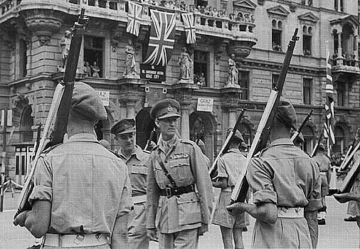 Der General McCreery in Graz in Uniform mit Kappe zwischen einigen britischen Wachsoldaten vor dem Rathaus, das mit einigen Union Jacks beflaggt ist. 