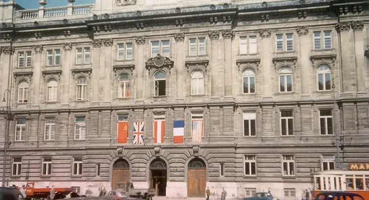 Blick auf das Gebäude mit einigen Autos im Vordergrund. Die Flaggen der Alliierten und Österreichs sind über dem Eingang nebeneinander aufgespannt.