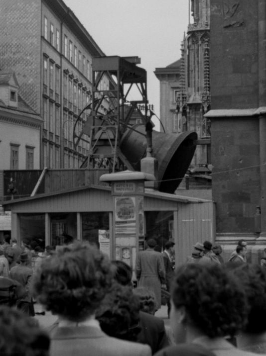 Die Pummerin, die große Glocke des Stephansdoms, die noch neben dem Turm aufgestellt ist, läutet zum freudigen Ereignis. Menschenmenge neben dem Stephansdom beim Gerüst auf dem die Glocke läutet.