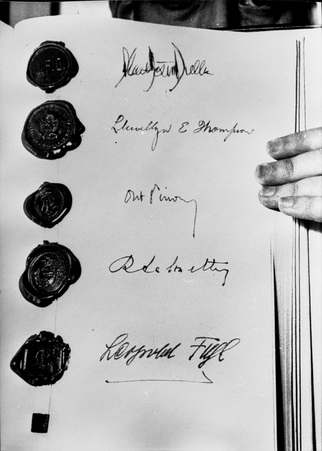 Zoom: Vertragsseite mit Teil einer Hand die zum Mann gehört, der das Vertragsbuch aufgeschlagen in die kamera hält.
