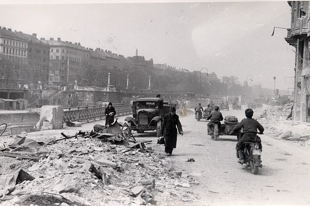 Straße am Donaukanal mit Schutt, LKW einigen Fußgängern und sowjetische Soldaten auf Beiwagenmotorädern.