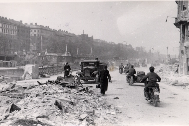 Straße am Donaukanal mit Schutt, LKW einigen Fußgängern und sowjetische Soldaten auf Beiwagenmotorädern.