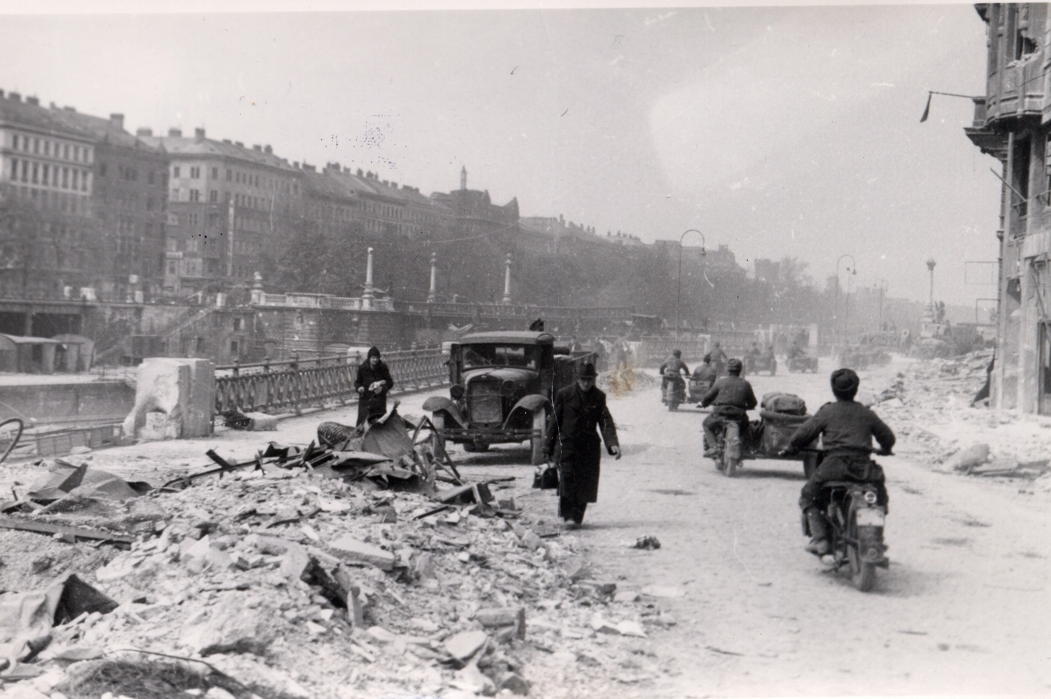 Straße am Donaukanal mit Schutt, LKW einigen Fußgängern und sowjetische Soldaten auf Beiwagenmotorädern.