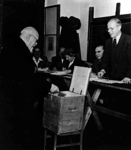 Bundespräsident Karl Renner. Einwerfen des Stimmzettels in eine hölzerne Urne vor Männern der Wahlkommission.