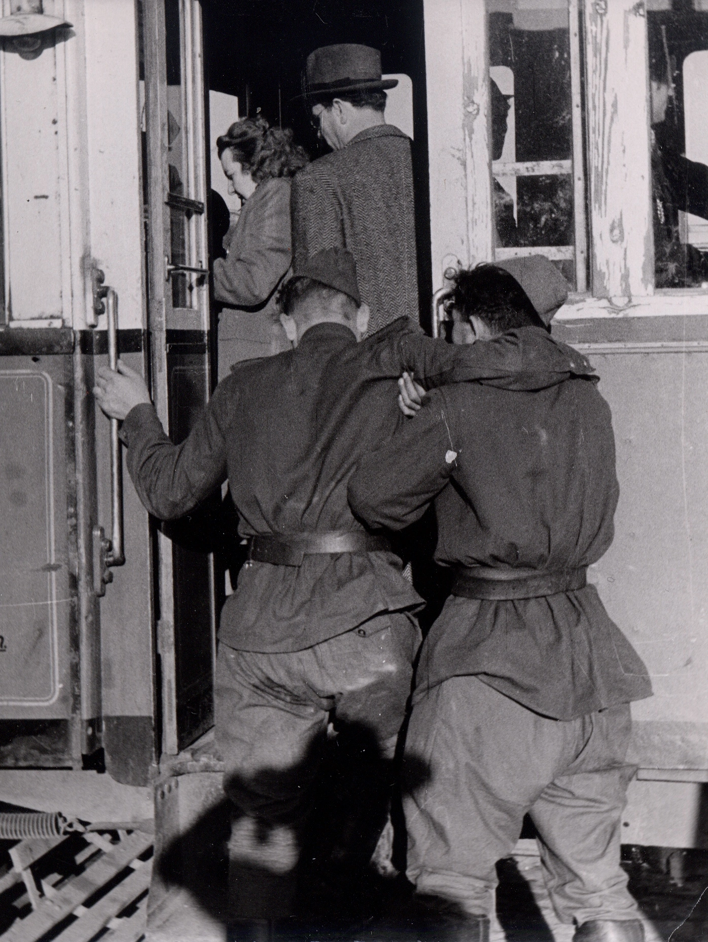 Rückenansicht der beiden Soldaten. Der eine hilft dem anderen - schwer beeinträchtigten - in die Straßenbahn hinauf.
