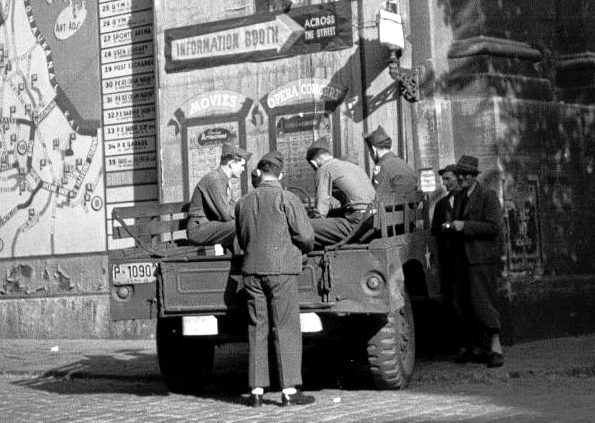 Informationsplakat an einer Brücke in Wien. Soldaten auf einem stehenden Militär-PKW zu sehen.