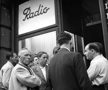 Männer hören vor einem Radiogeschäft mit ernster Mine der Radioreportage zu.