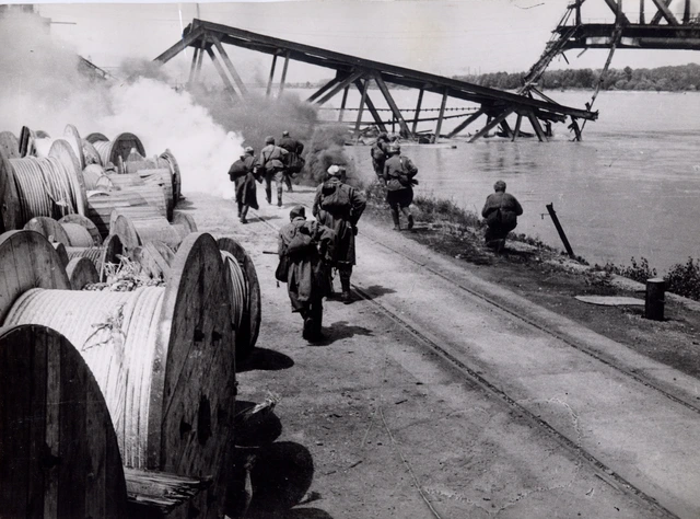 Soldaten am Donauufer. Im Hintergrund eine zerstörte Brücke.