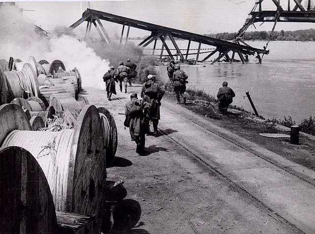 Soldaten am Donauufer. Im Hintergrund eine zerstörte Brücke.