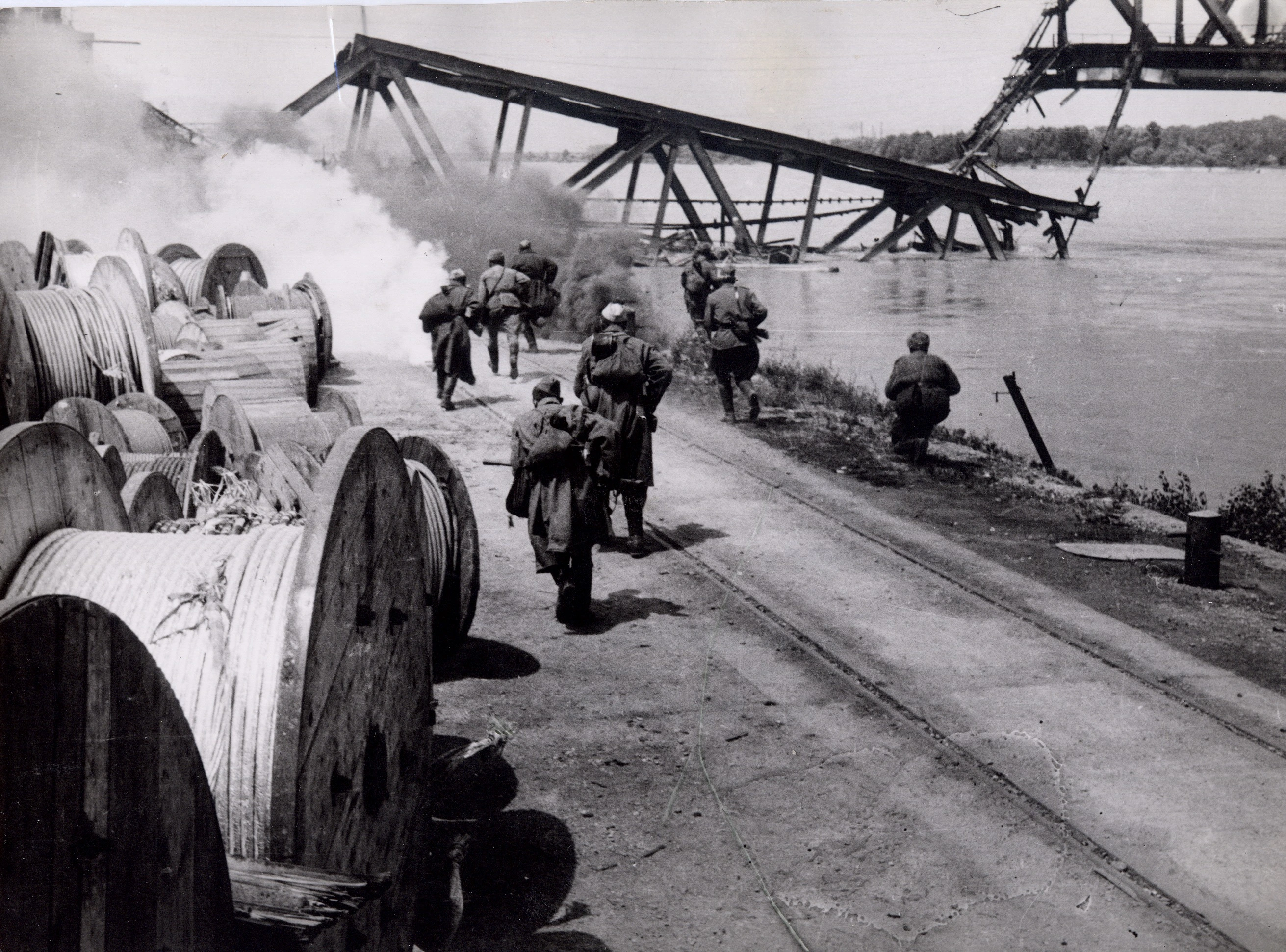 Soldaten am Donauufer. Im Hintergrund eine zerstörte Brücke.