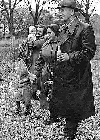 Frauen mit Kindern und ein Mann mit einem Babyflascherl gehen über ein Feld.
