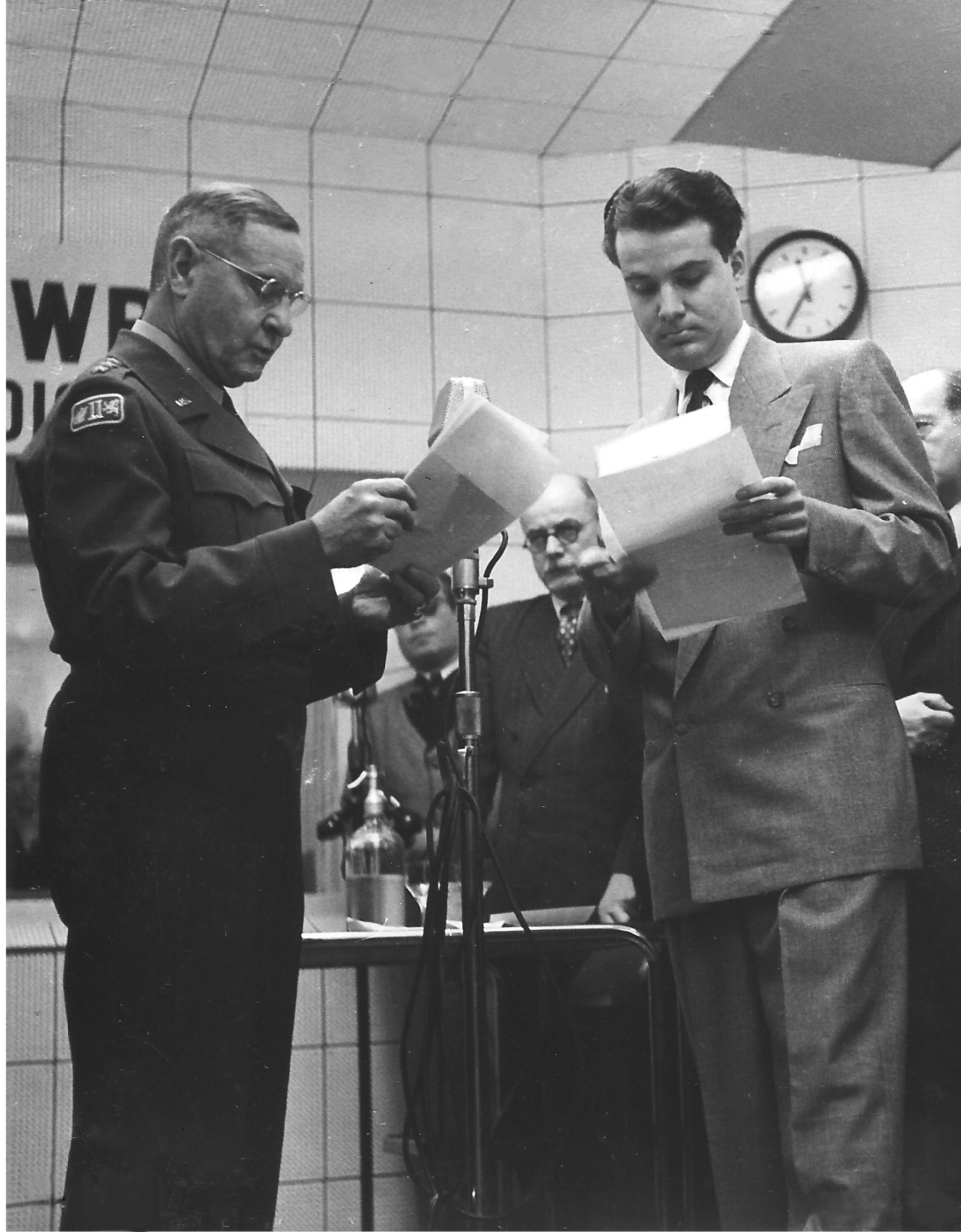 General Geoffrey Keyes vor einem Mikrofon im hellen Radiostudio in Uniform stehend.