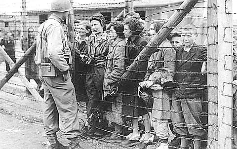 Frauen und Kinder sprechen mit einem US-Soldaten. Unterhaltung durch den Stacheldrahtzaun des Konzentrationslagers