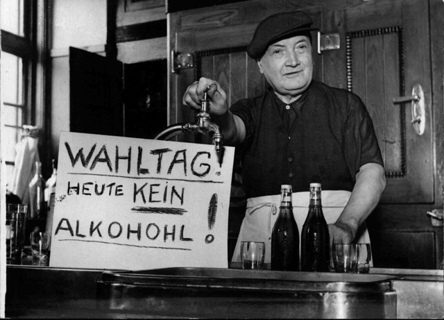 Ein Wirt an der Schank mit einem selbstgeschriebenen Schild: "Wahltag heute kein Alkohohl (sic)!