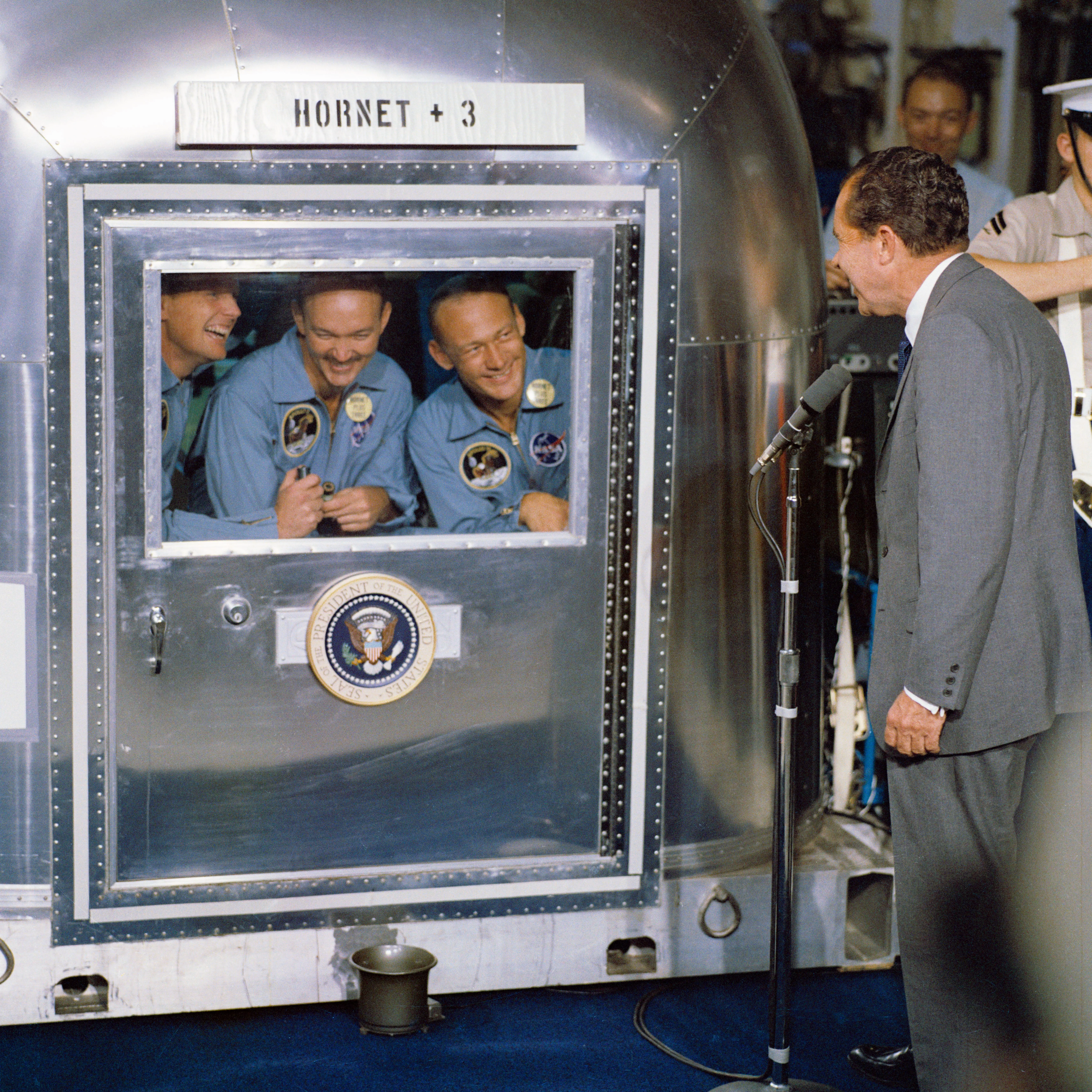 Die Mannschaft von Apollo 11 nach der Rückkehr in Quarantäne - US-Präsident Nixon vor dem Qurantänrebehälter