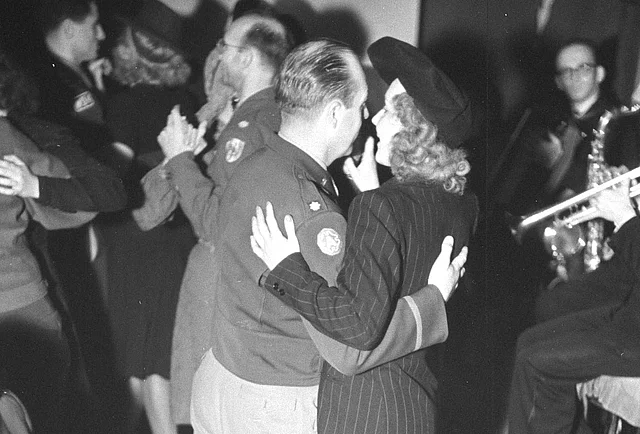 Tanzende US-Soldaten in Uniform mit eleganten Damen. Rechts ist die Musikgruppe erkennbar.