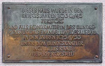 Informationstafel, die auf wiedererichteten Gebäuden angebracht wurde. Text: "Dieses Haus wurde in den Kriegsjahren 1939/45 zerstört und aus Fondsmittel des Mundesministeriums f. Handel u. Wiederaufbau in den Jahren 1954/55 unter Bundeskanzler Ing. Julius Raab wiederhergestellt"