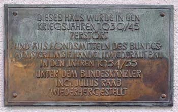 Informationstafel, die auf wiedererichteten Gebäuden angebracht wurde. Text: "Dieses Haus wurde in den Kriegsjahren 1939/45 zerstört und aus Fondsmittel des Mundesministeriums f. Handel u. Wiederaufbau in den Jahren 1954/55 unter Bundeskanzler Ing. Julius Raab wiederhergestellt"