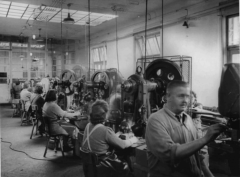 Frauen und ein Mann in einer kleineren Fabrikshalle mit Wekbänken an denen sie arbeiten