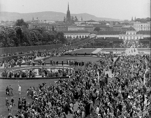 Jubelnde Menge vor dem Belvedere, im Park, nach der Unterzeichnung. Im Hintergrund bzw. am Horizont der Stephansdom.