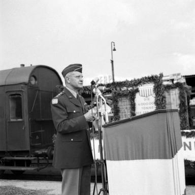 US-General Keyes hinter einem Podium, das an den Gleisen aufgestellt ist. Ein Personenwaggon ist hinter ihm zu sehen.