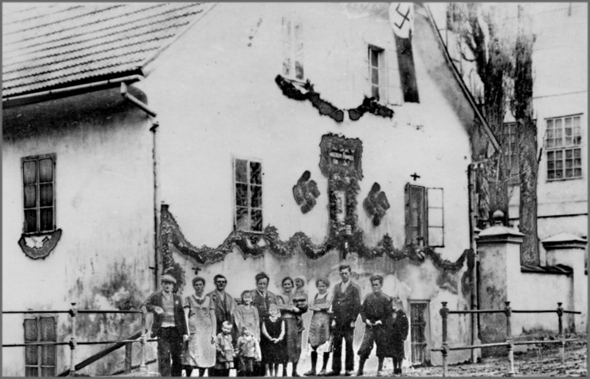 Vor einem Haus in Weißenbach bei Gloggnitz, das anlässlich der Volksabstimmung mit Hakenkreuzen und Hakenkreuzfanhen geschmückt ist, stehen einige Personen.