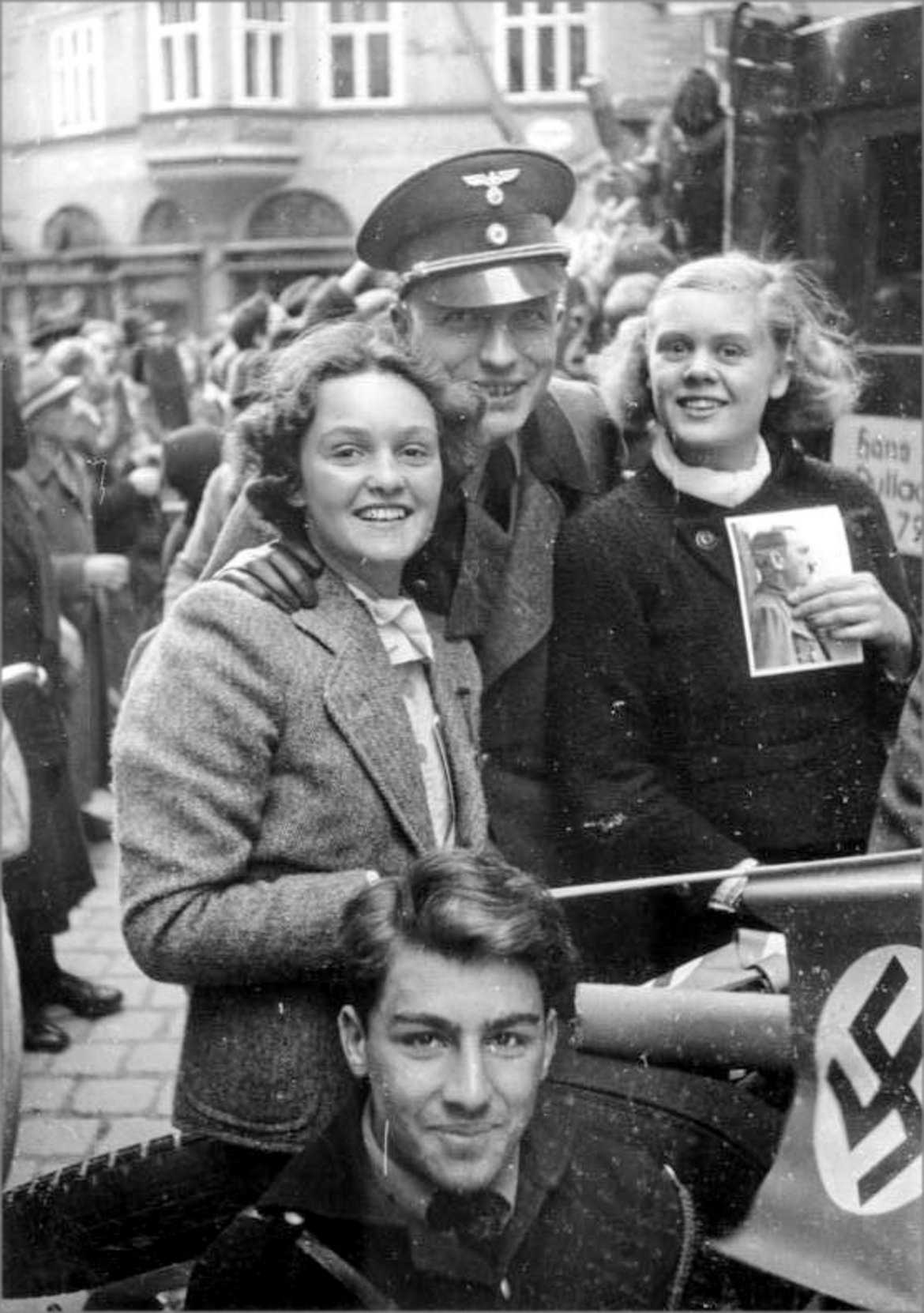 Zwei junge Frauen, Hakenkreuzfähnchen und Hitlerporträt in der Hand, mit deutschen Soldaten am 13. März 1938 in Salzburg.