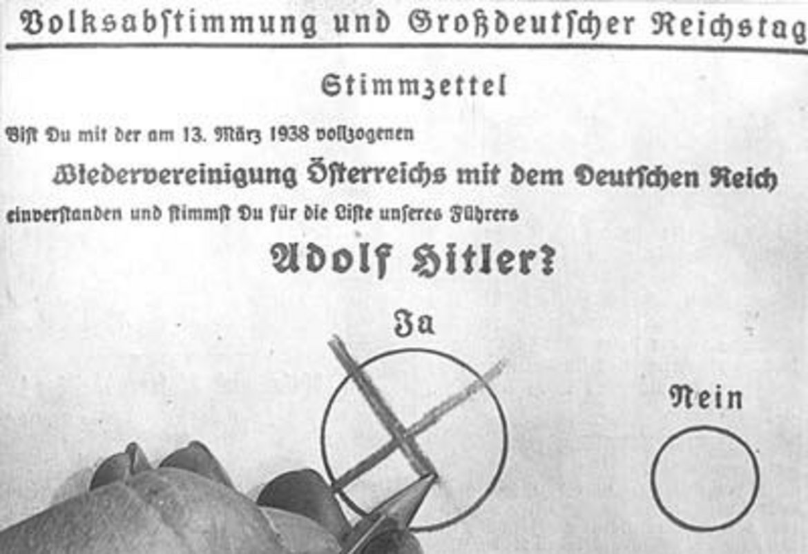 Es ist eine Hand zu sehen, die auf dem Stimmzettel für die Volksabstimmung 1938 mit einem Stift ein Kreuz in dem großen Kreis für "Ja" macht. Daneben ist ein deutlich kleinerer Kreis für "Nein".
Der Text auf dem Stimmzettel lautet: "Volksabstimmung und Großdeutscher Reichtag - Stimmzettel - Bist Du mit der am 13. März 1938 vollzogenen Wiedervereinigung Österreichs mit dem Deutschen Reich einverstanden und stimmst Du für die Liste unseres Führers Adolf Hitler - Ja - Nein".