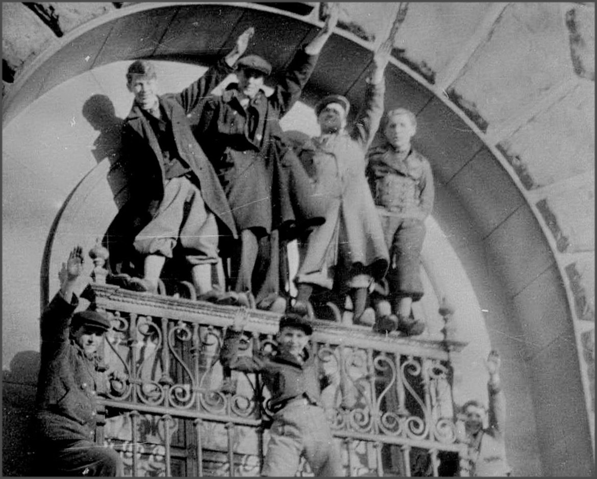 Einige Personen stehen auf einem Fenstergitter an der Neuen Hofburg und strecken die rechte Hand zum Hitlergruß in die Höhe.