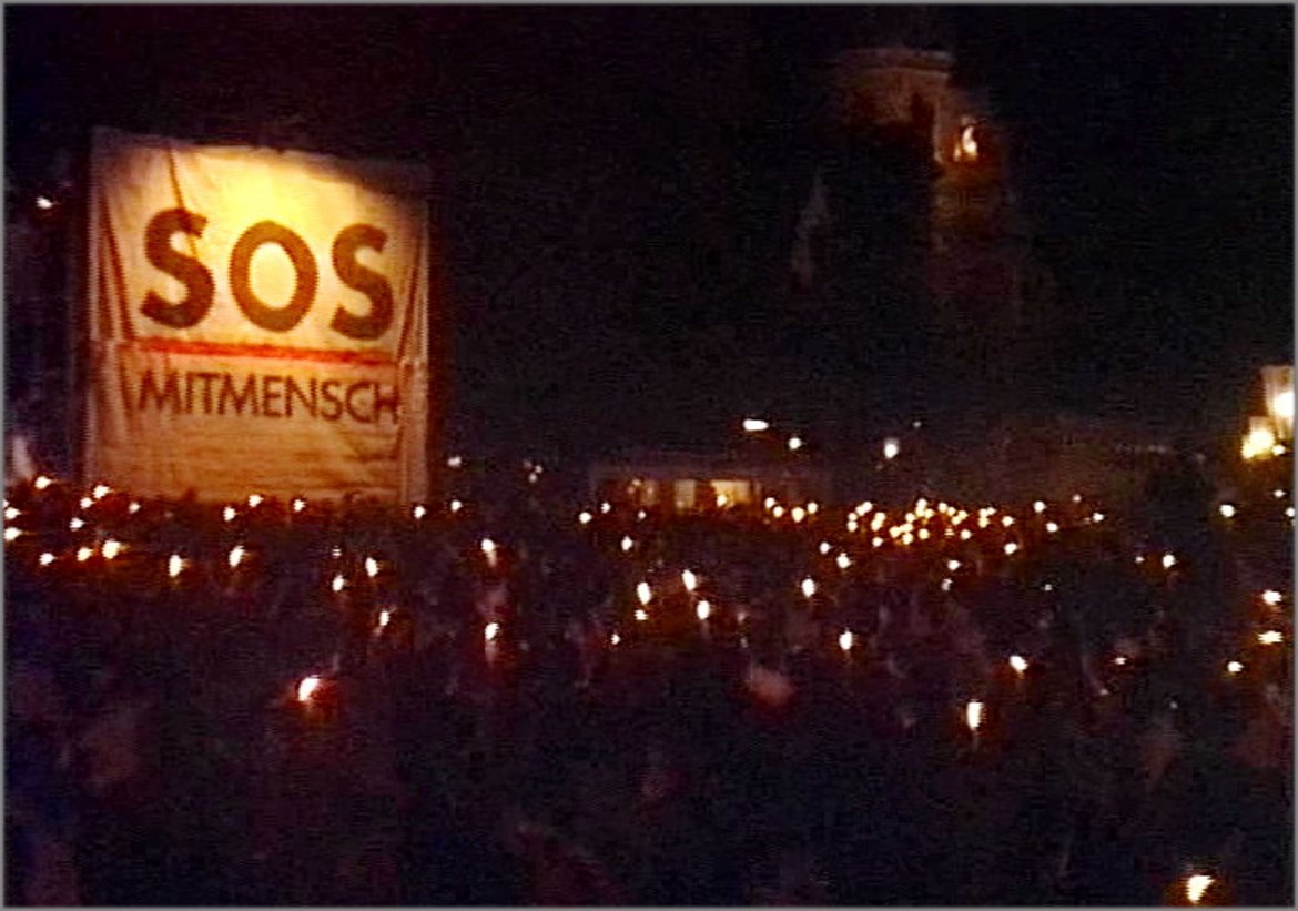 Foto vom Lichtermeer. Zu sehen sind viele Fakeln vor der Bühne mit einem großen Transparent mit der Aufschrift "SOS Mitmensch".