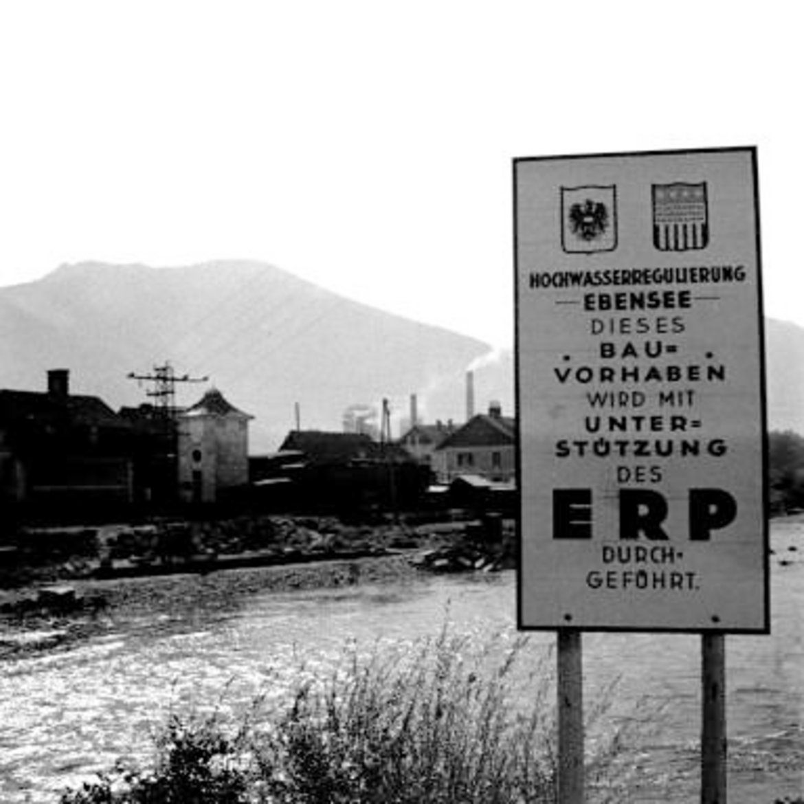 Schild am Flussufer mit US-Wappen und österr. Bundesadler und der Aufschrift: Hochwasserregulierung Ebensee. Dieses Bauvorhaben wird mit Unterstützung des ERP durchgeführt"